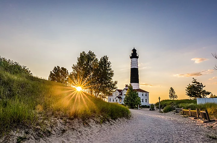 Phare à proximité d’une colline verdoyante sur laquelle le feuillage des arbres laisse passer les rayons du soleil, ce qui crée un halo