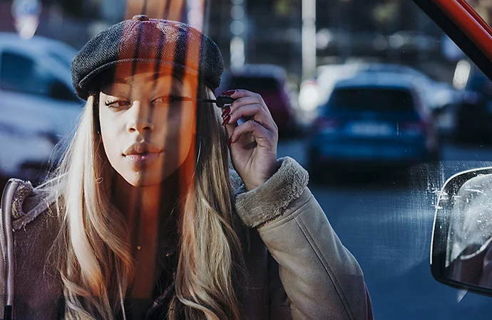 Photo sur le vif du reflet dans une vitre de voiture d’une femme appliquant du mascara
