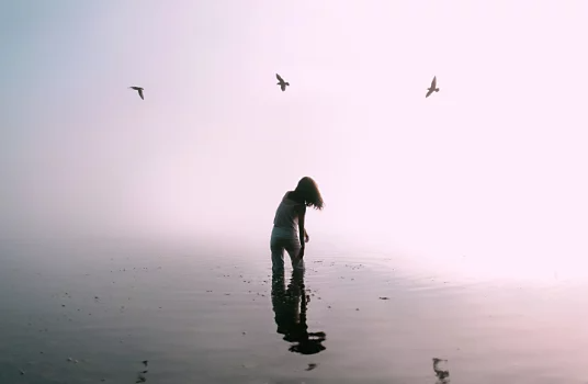 Personne debout dans une eau peu profonde avec trois oiseaux qui volent au-dessus d’elle