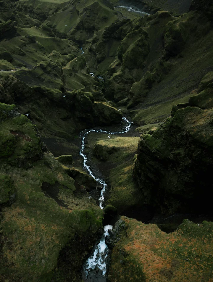 Eaux vives et écumantes d’un ruisseau divisant une luxuriante vallée verdoyante en deux, photographiées depuis les airs