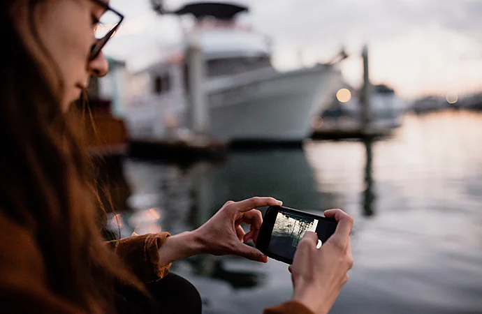 Photo prise avec un smartphone d’une photographe debout près du rivage, observant l’écran de son reflex numérique