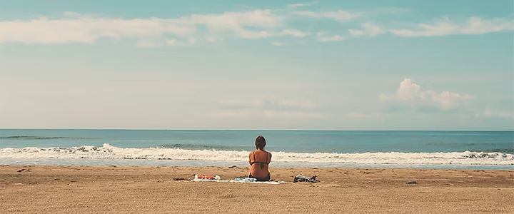 Plan large d’une personne assise seule regardant l’océan, permettant de situer la scène