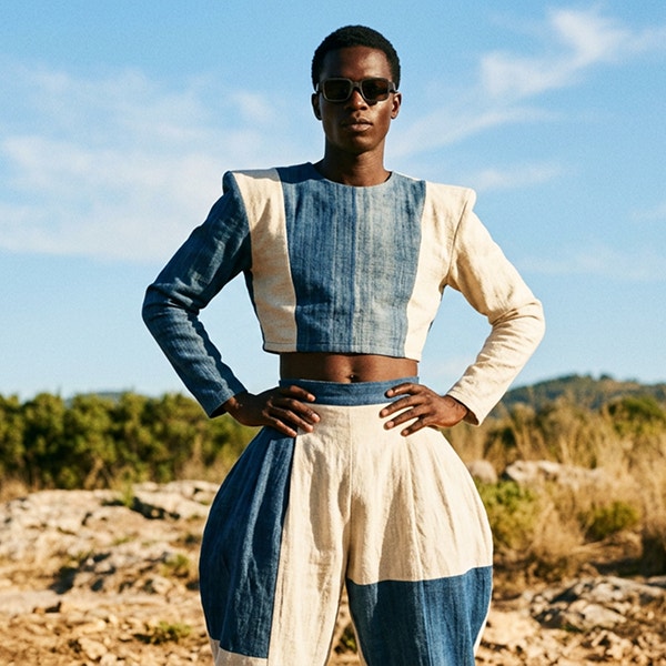Un mannequin portant des lunettes de soleil et une tenue sculptée bleu et blanc se tient en extérieur, sous un ciel dégagé, dans un paysage naturel.