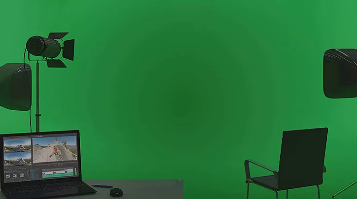 A greenscreen fills the background with a laptop ready to select different backgrounds using Adobe's green screen software