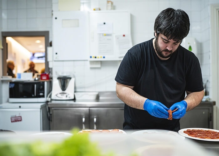 A pizza artist wearing gloves and topping a pizza