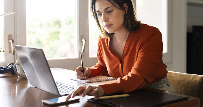 A person takes notes based on the content they are reading on their smartphone