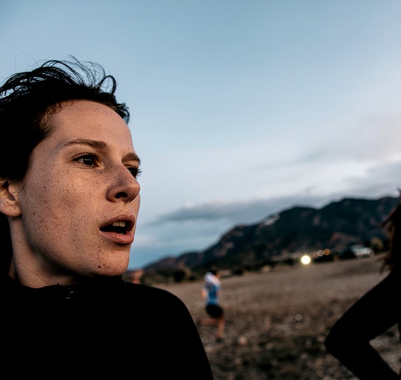 A close-up shot of two women running through a field with hills in the background.