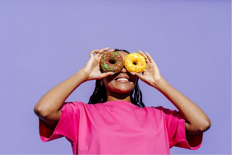 Image of a woman holding donuts to her eyes and a purple background