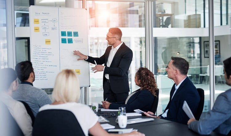A man meeting with staff at a whiteboard in the office, discussing workflow steps, diagrams, or teamwork for web design.