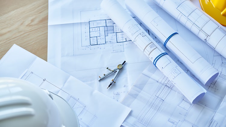 Printed construction files, blueprints, and safety helmets on a wooden table.