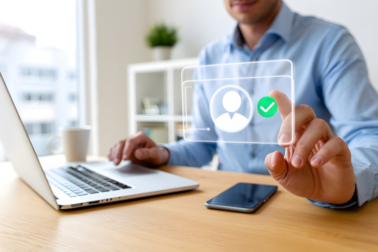 Person completing digital KYC verification on a touchscreen interface, with a laptop and smartphone on the desk.