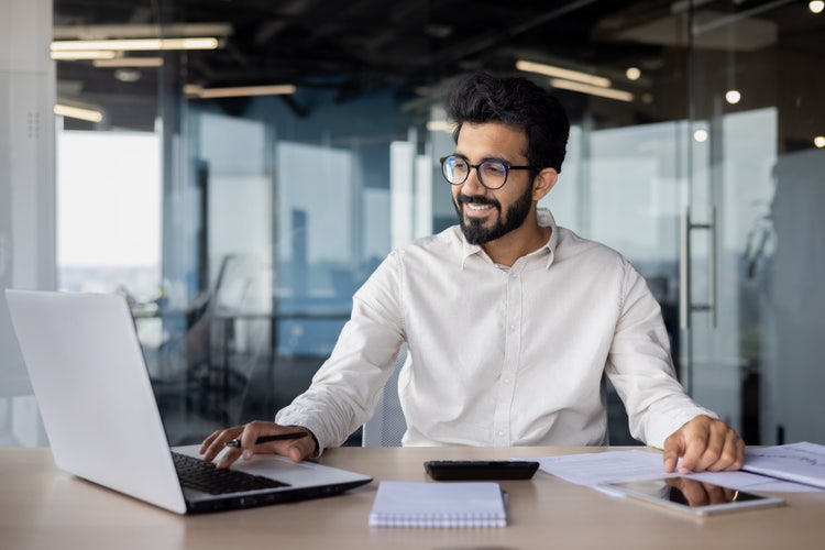 Business professional using laptop and papers in modern office, leveraging AI for efficiency