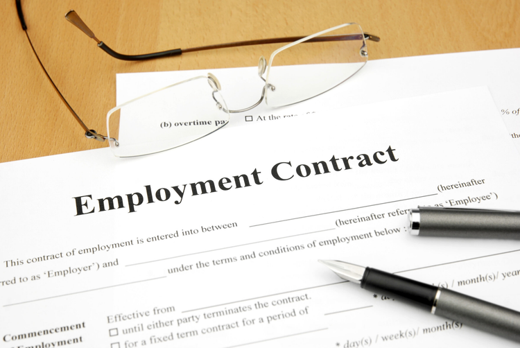 Portion of a paper copies of an employment contract on a desk with reading glasses and a pen.