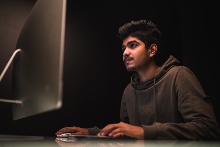 Young man working on a desktop computer in a dark room, focusing on how to password protect sensitive PDF files.