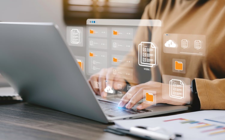 A young professional working on a laptop with several digital files and folders jumping off the screen.