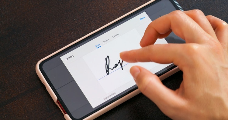 Person's hand signing an electronic document on the screen of a mobile phone.