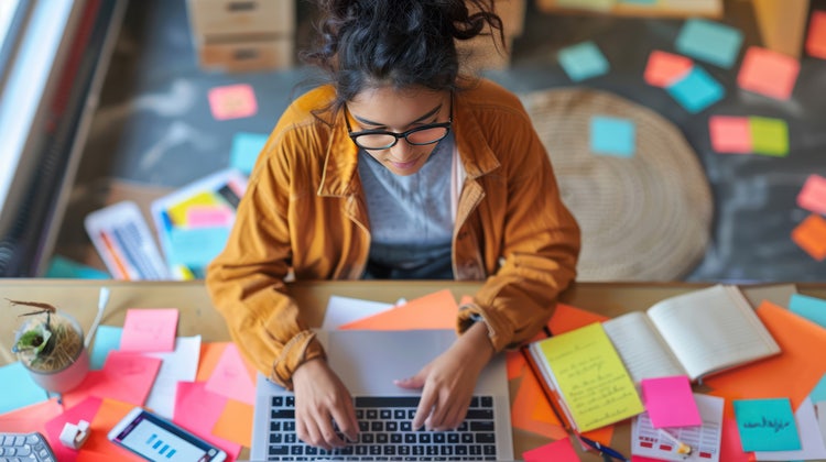 A university student engaged in an online discussion on social media, with a laptop open to a study forum and study notes spread around.