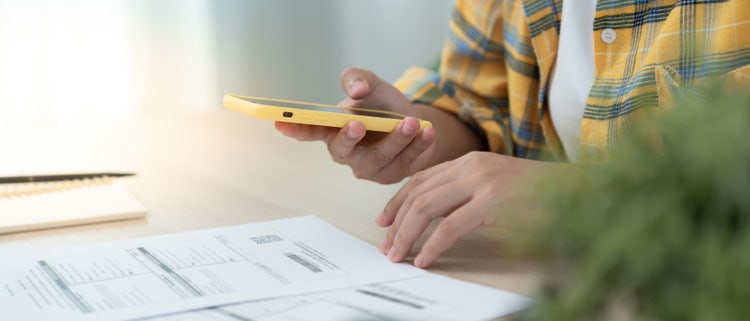 A young professional using their mobile phone to scan a UPI QR code from a printed PDF invoice.