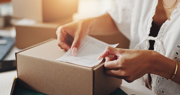 Small business owner affixing a purchase order label to a cardboard shipping box, preparing it for delivery.
