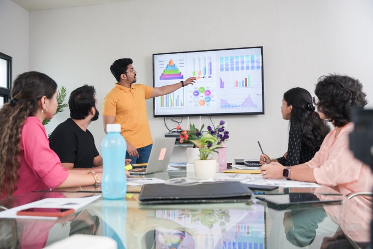 A young professional presenting a report with charts and graphs in a meeting room with colleagues.