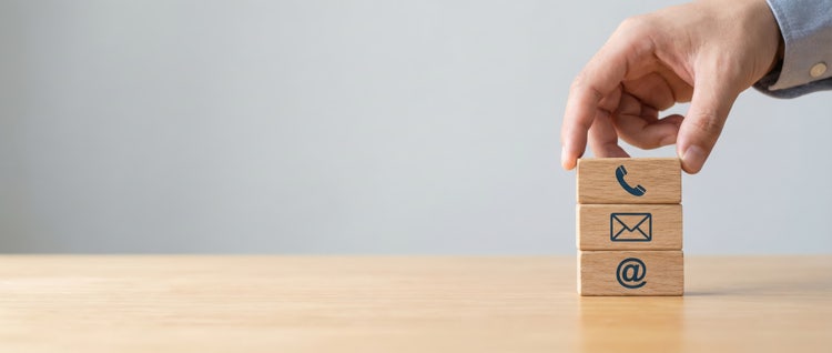 Hand stacking wooden blocks with phone, email, and at icons for graphic designer portfolio PDF contact info.