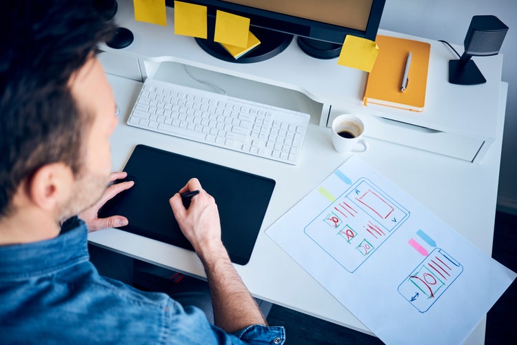 Graphic designer creating website layout sketches for graphic design portfolio examples on tablet at desk.