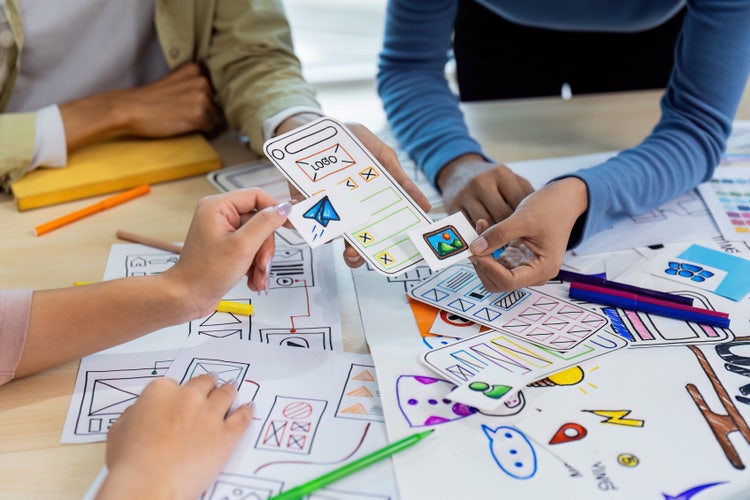 UI /UX designer team collaborating on mobile app wireframes with colourful paper prototypes and sketches.