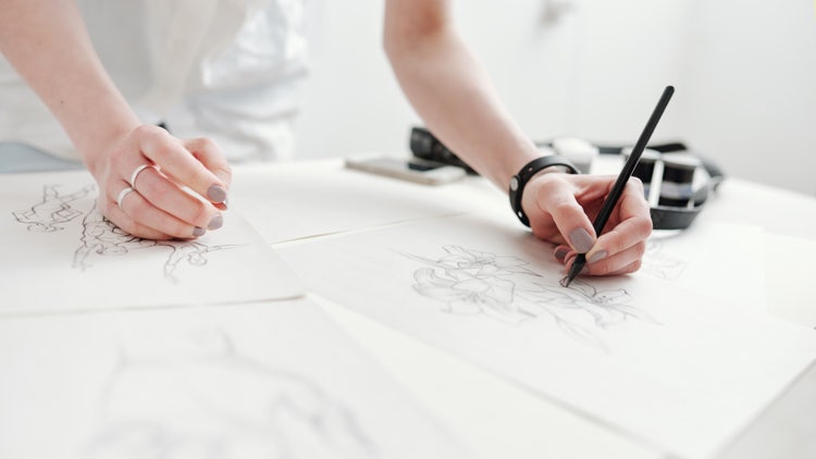 Hands sketching floral and figure drawings, showing how to become an illustrator through practice and skill development.