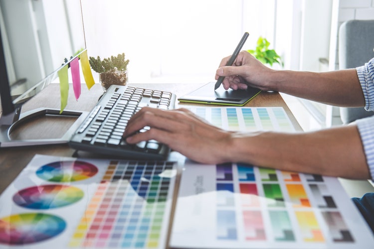 Visual designer working at desk with colour swatches, keyboard, and graphic tablet for digital design.