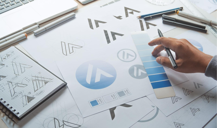 Person working on graphic design logo sketches, color swatches, and branding concepts at a desk.