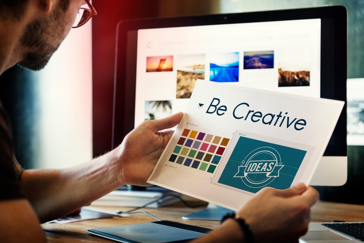Designer working on brand identity design with color palette and logo mockup at desk.