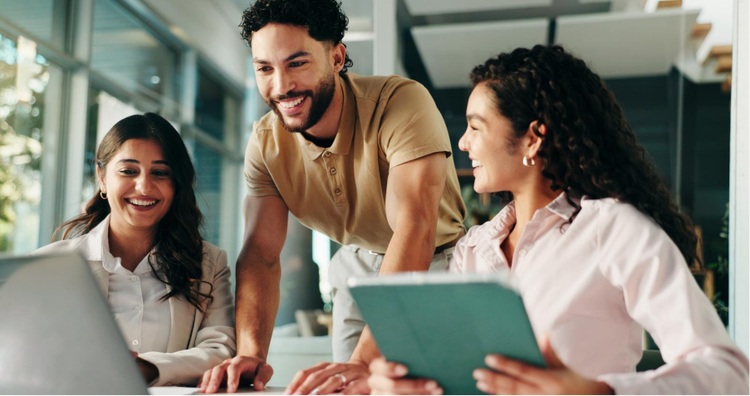 Three creative professionals collaborating in a bright office, reviewing a brand guide on a laptop and tablet during a design planning session.
