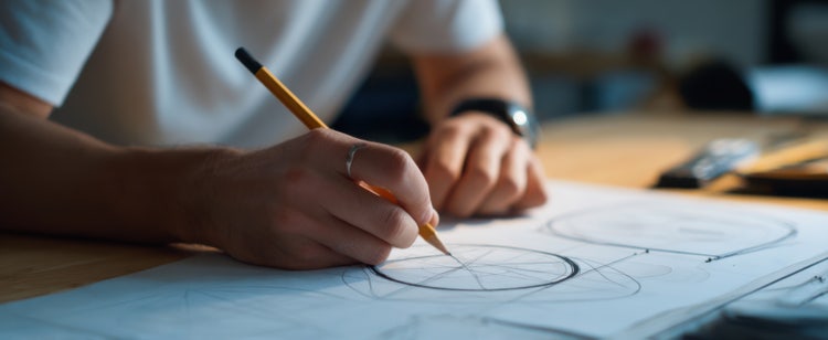 Hands holding a pencil and creating design sketches, highlighting foundational skills needed for graphic designers in India.