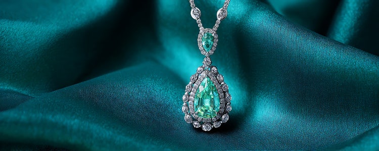 Elegant emerald and diamond necklace displayed on teal satin fabric, with a subtle drop shadow enhancing its depth and sparkle.