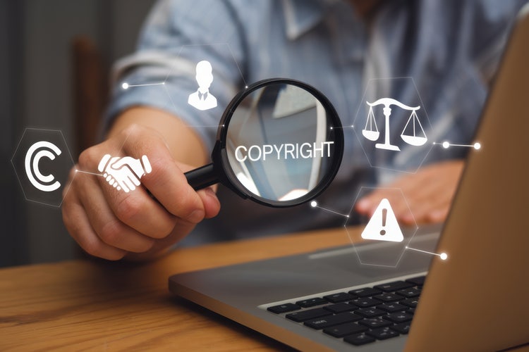 Magnifying glass highlighting 'COPYRIGHT' with digital legal icons on a laptop screen.