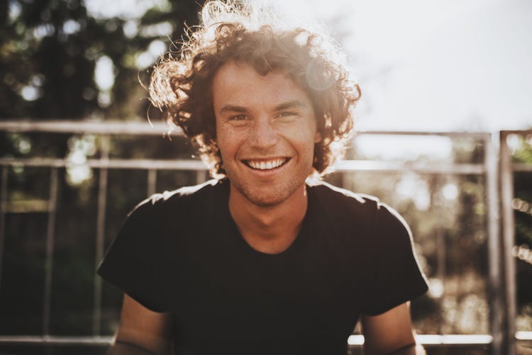 Outdoor closeup portrait of handsome freckled smiling male with curly hair.