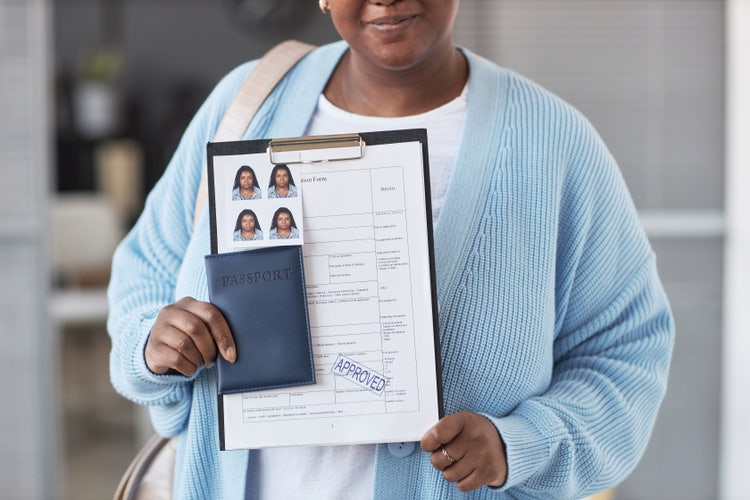 A woman holding a clipboard with her passport photos, documents, and passport.