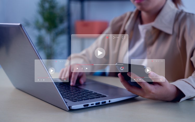 Person using a laptop and smartphone to watch video content, symbolising online learning through Photoshop tutorials across multiple devices.