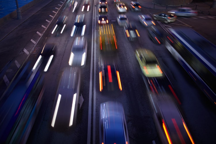 Long exposure night photograph of moving cars with motion blur, capturing dynamic light trails in a city setting.