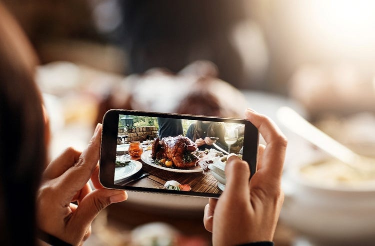Close-up of a person using an iPhone to take a professional-grade photo of a cooked turkey, presented on a table.