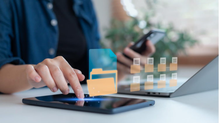 A person accessing a digital file on their table while using their phone and having multiple digital files open on the laptop.