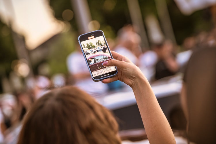 Person capturing a moment with a smartphone in a busy outdoor setting, illustrating the concept of converting Live Photos to video for sharing.