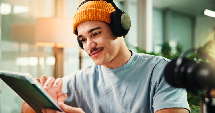 Image of a young content creator wearing headphones and editing a video on a tablet, designing lower third graphics for a branded clip.