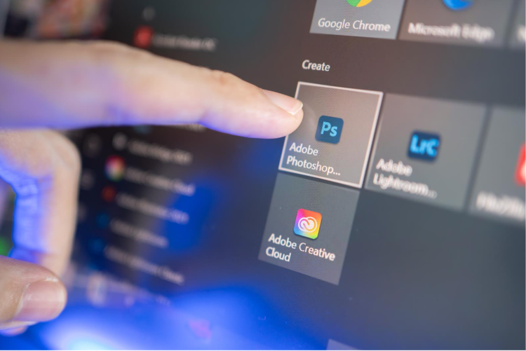 A human finger clicking on the Adobe Photoshop icon on a laptop screen.