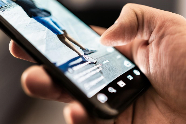 A hand holding a mobile phone, scrolling through social media videos.