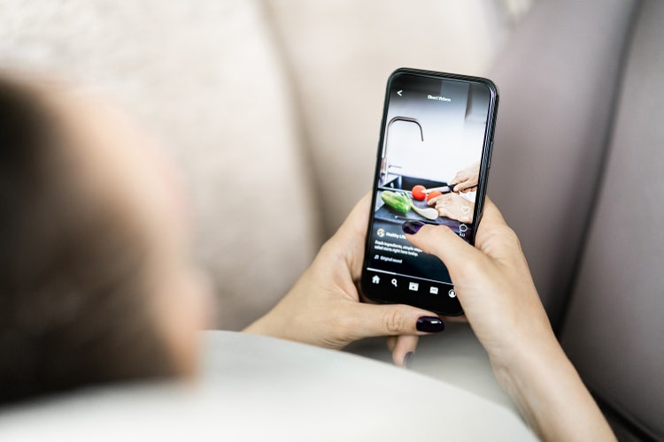 A pair of hands holding a mobile phone displaying a short video clip on social media.