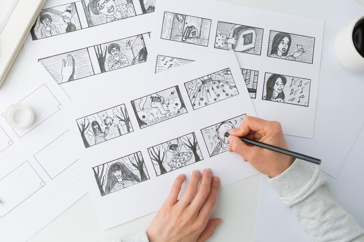 The hands of an illustrator holding a pencil and sketching the visuals for a storyboard.
