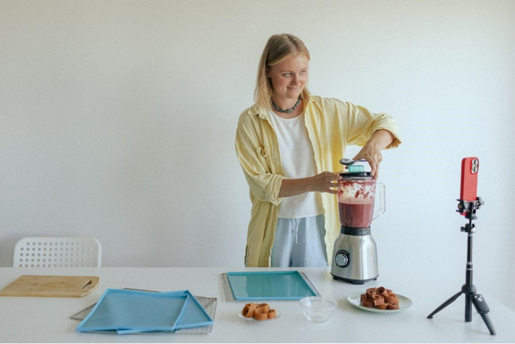 A woman filming herself preparing homemade fruit leather in her kitchen.