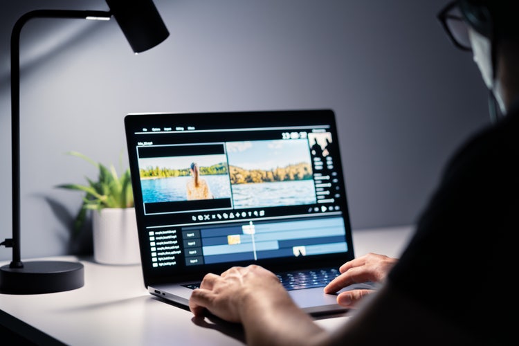An amateur artist working on a video editing software on a laptop atop a home desk with a lamp and a plant.