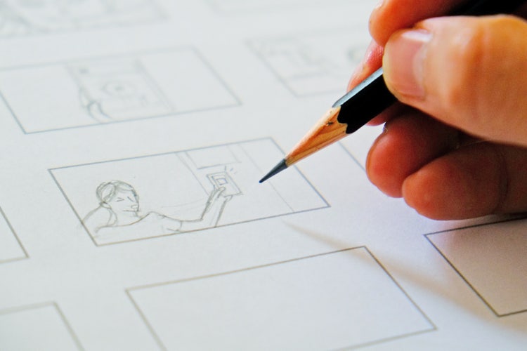 A close-up of a hand holding a pencil and sketching a storyboard for an explainer video.